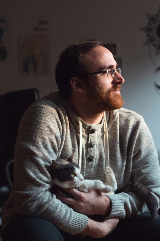 man in sweater holding a cat looking away from the camera