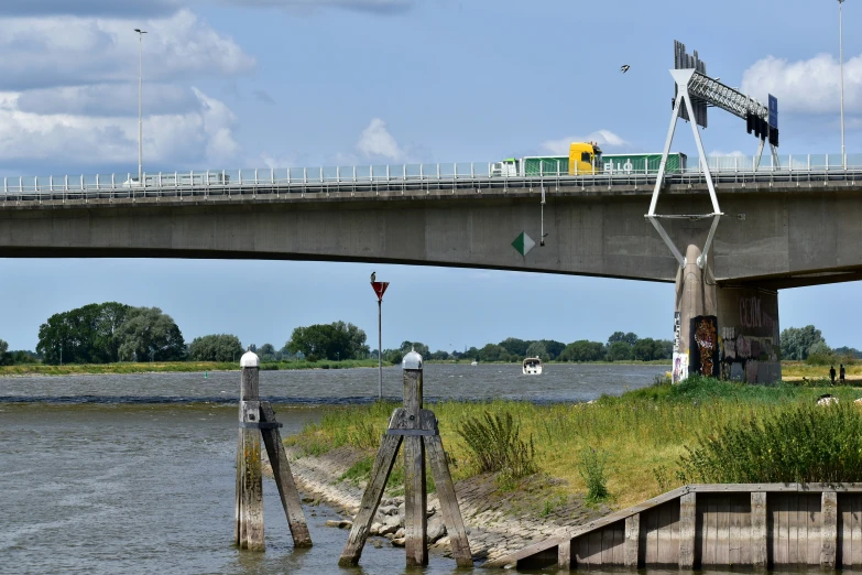 traffic signs sit on a pole on the river bank near a bridge