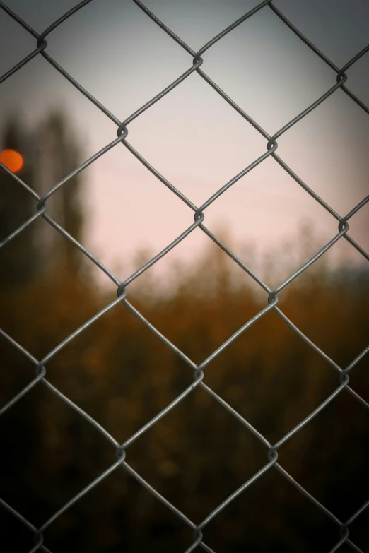 an orange dot shines through a chain link fence