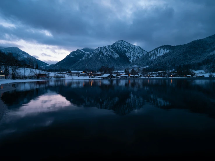 a lake sitting on the side of a snow covered mountain under cloudy skies