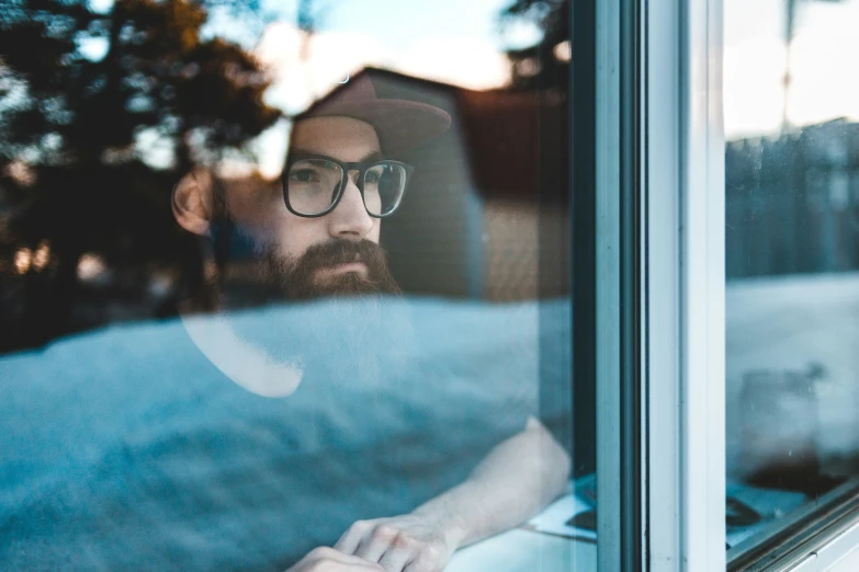 a man wearing glasses looking out of a window