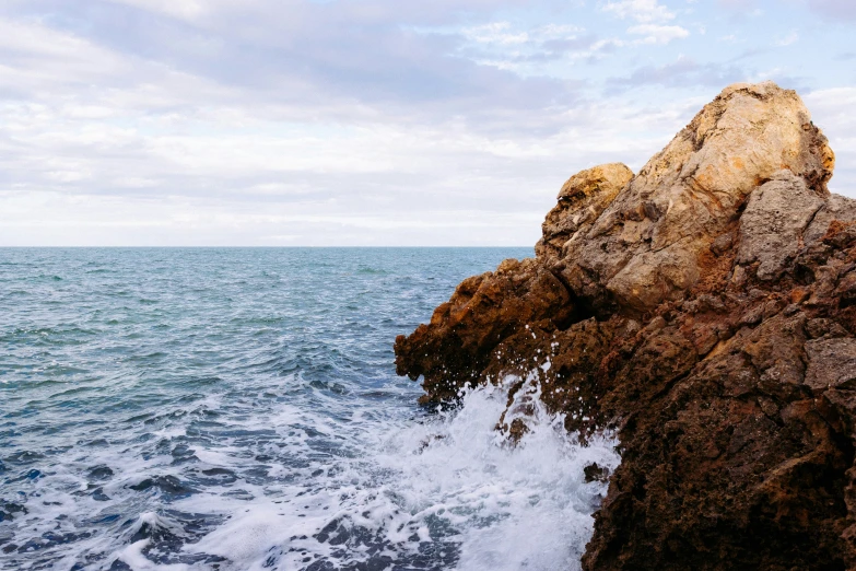 large rock sticking out of the ocean, with waves crashing against the rock