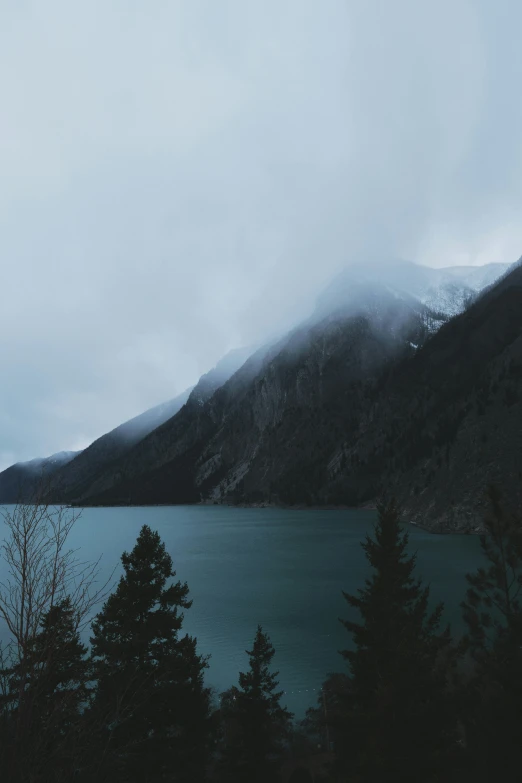 a foggy mountain and lake in a dark forest