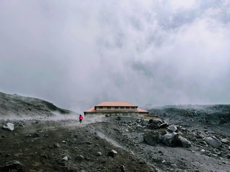 a man stands alone in the mountains as smoke is billowing from the roof