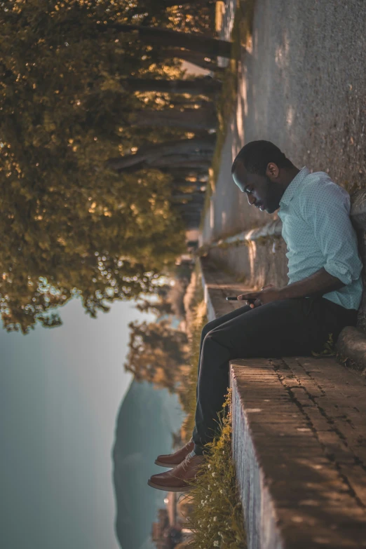 a man sitting on top of a wall near water