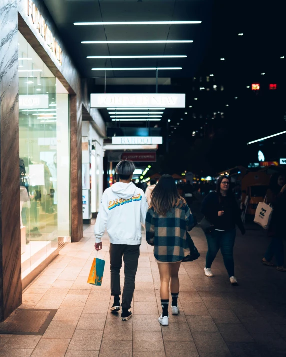 two people carrying bags are walking together down a sidewalk