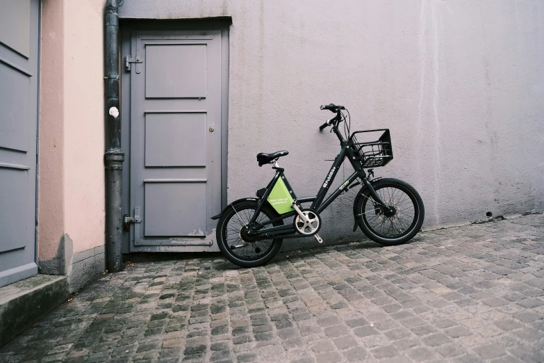 an adult bike with a basket sitting against a building
