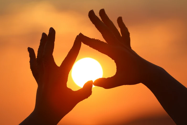 two hands raised to the sun with the sunset in the background