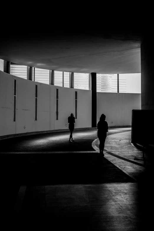 two people walking down a long hall with windows