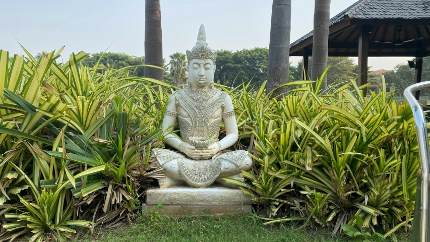 a statue in the middle of a field with some plants and trees