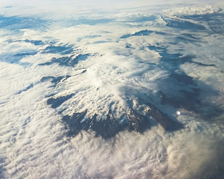 clouds cover a snowy mountain as it passes over the ocean