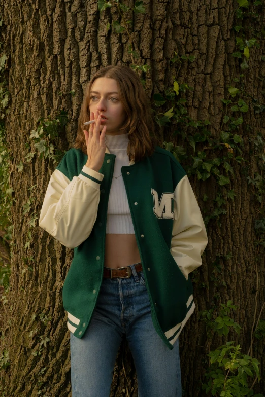 woman in green jacket smoking next to a tree