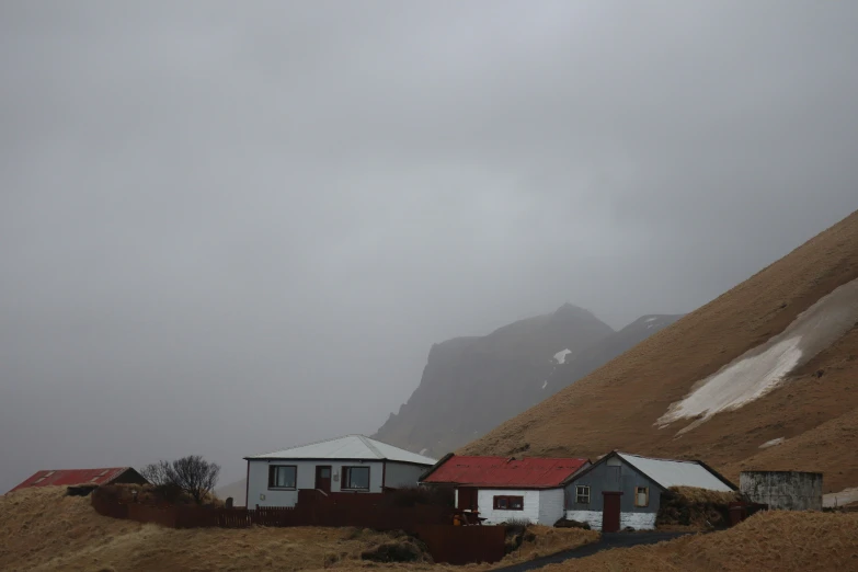 several houses in the distance, behind a steep hill with snowy mountains