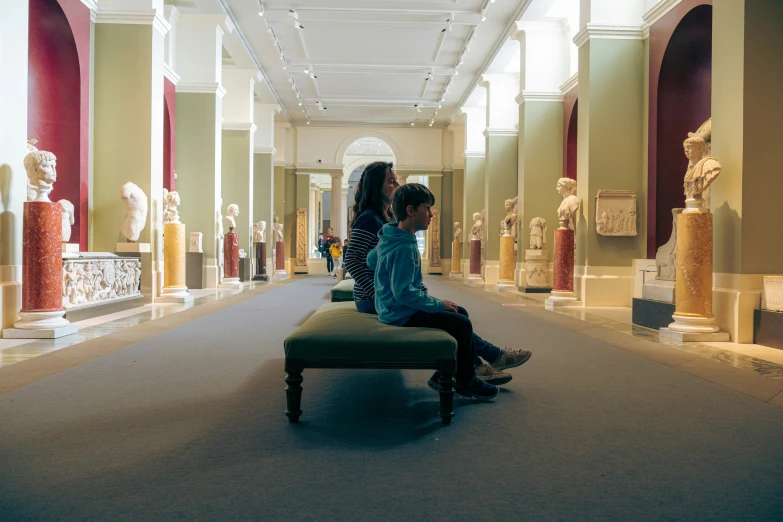 two young women sitting on a bench inside of a museum