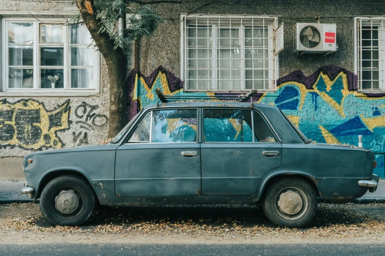 an old car parked near a wall covered in graffiti