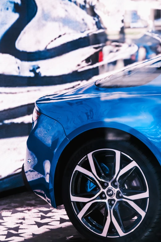 a blue car with big wheels sitting on a sidewalk