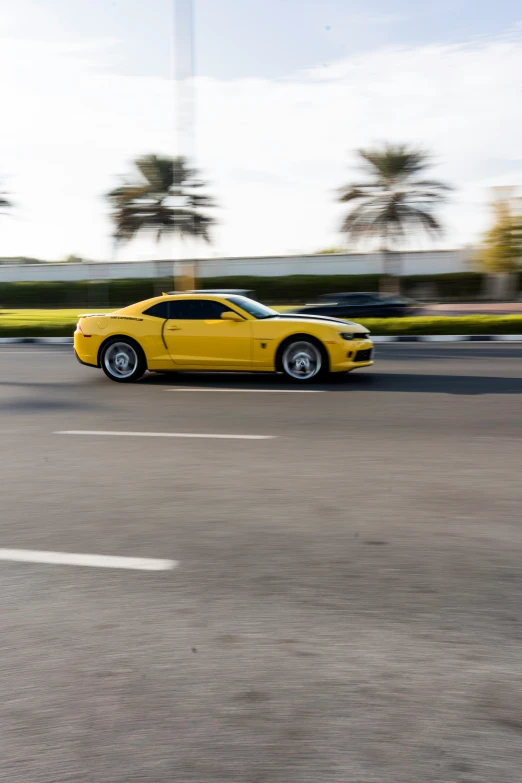 a yellow sports car is driving past some palm trees