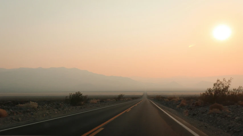 a car traveling down a long road with mountains in the background