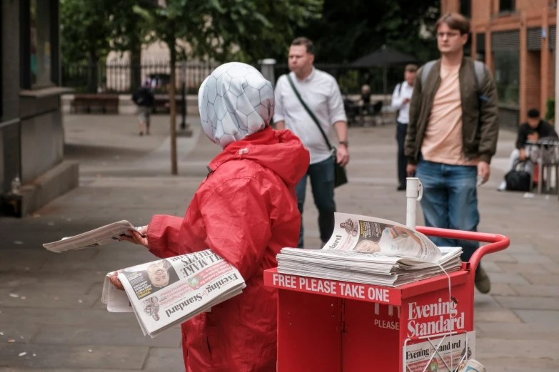 a man in a red rain coat standing next to newspaper