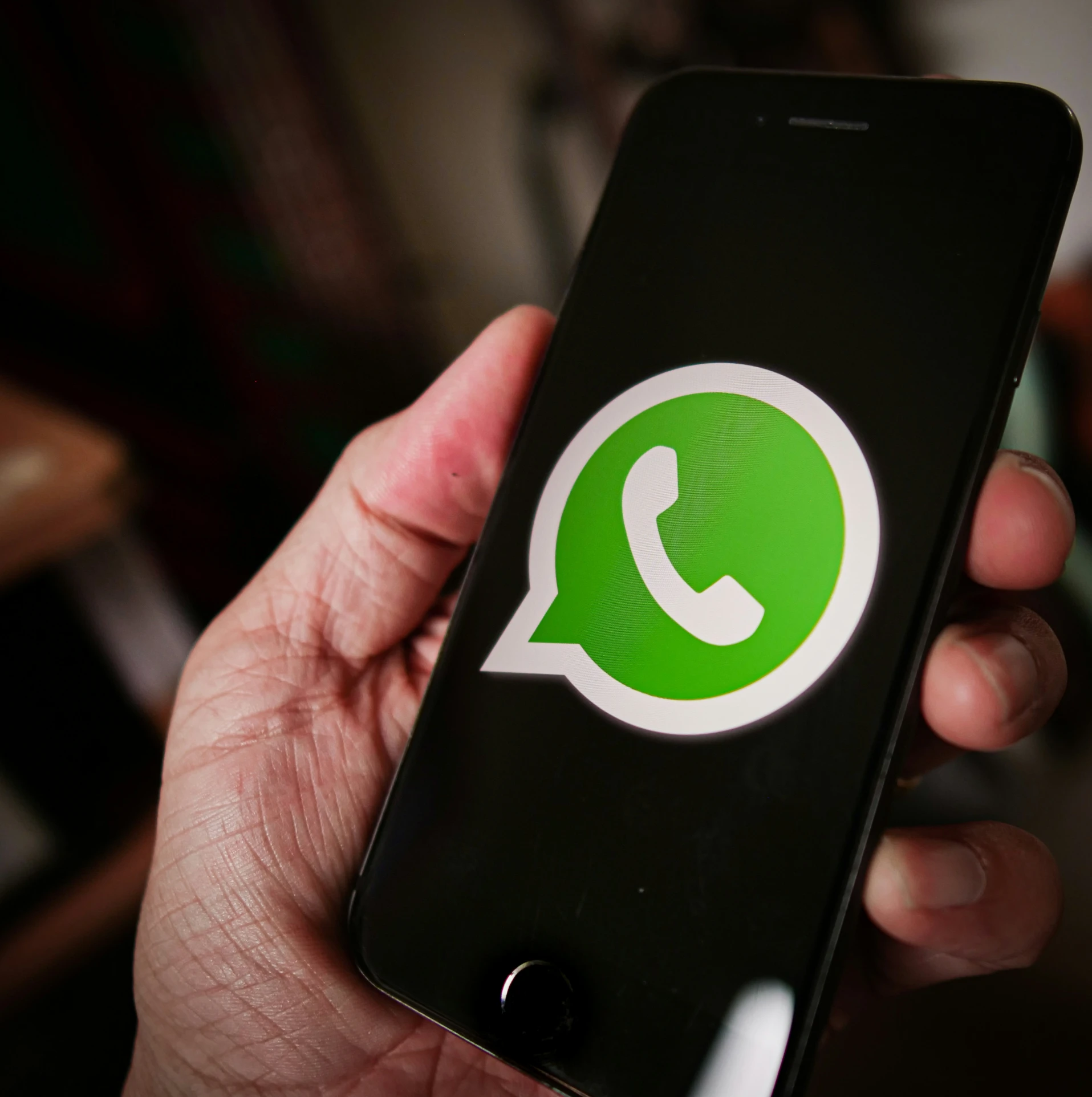 the person holds up their cell phone with the green whatsapp logo