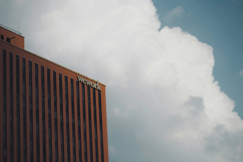 a brown brick building stands next to a white cloud filled sky