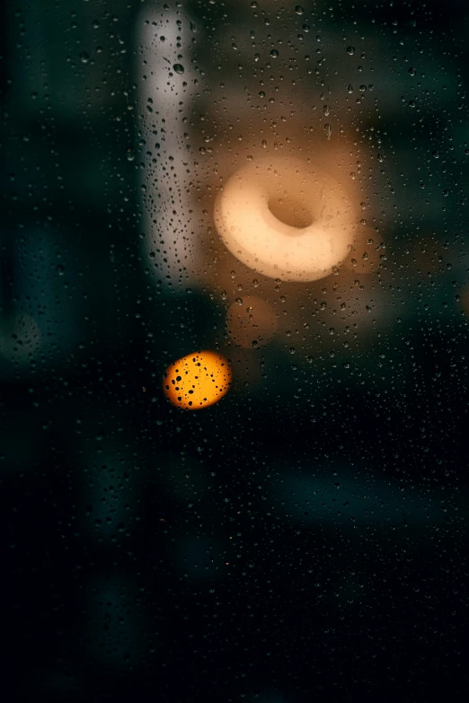 a yellow street sign seen through a window with rain