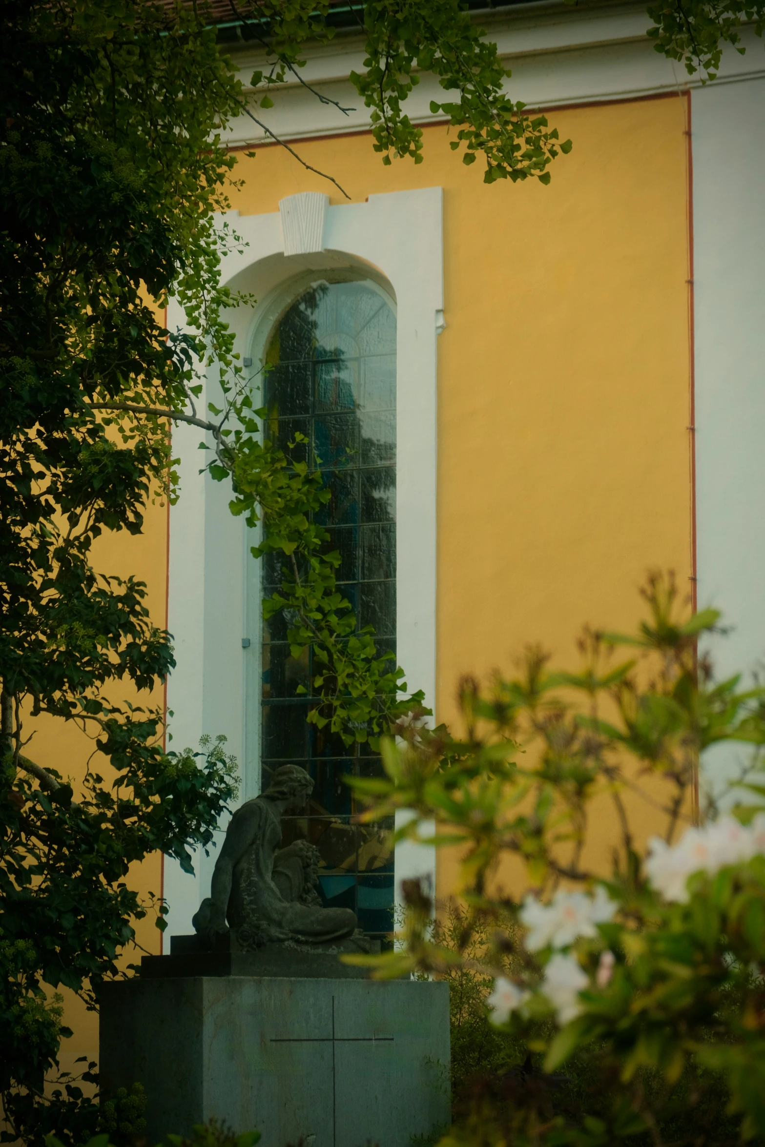 there is a statue near some trees and yellow wall