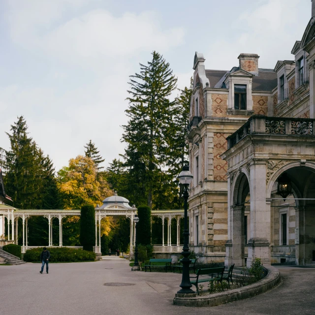 people in a garden with a stone building and many trees