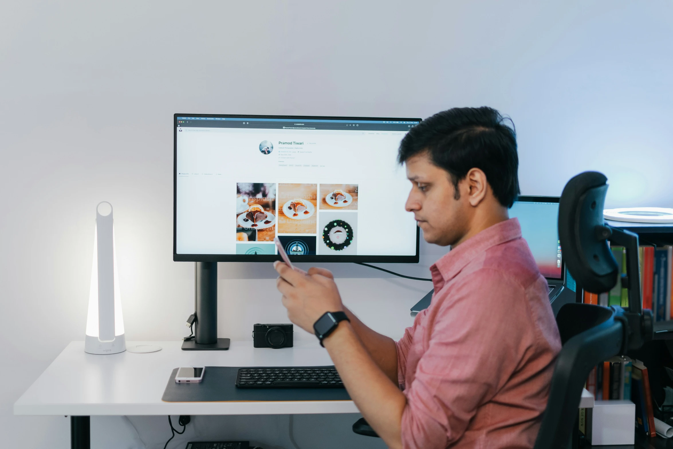 the man is using his phone and sitting in front of the computer