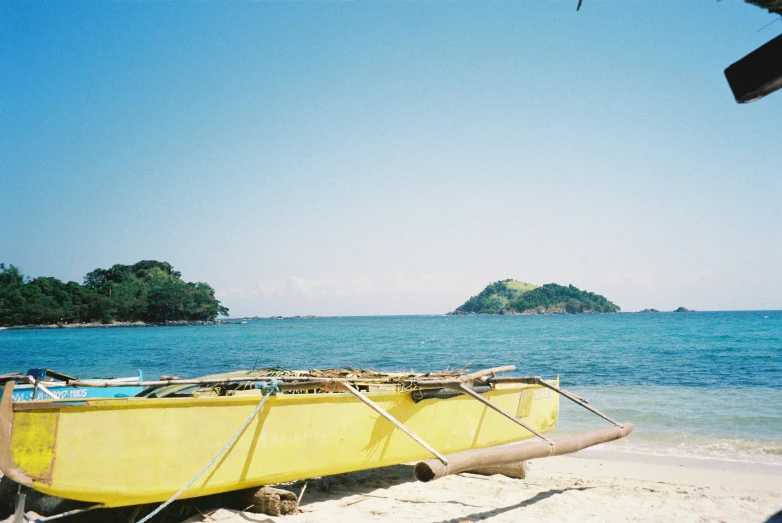 a yellow boat on the sand next to water