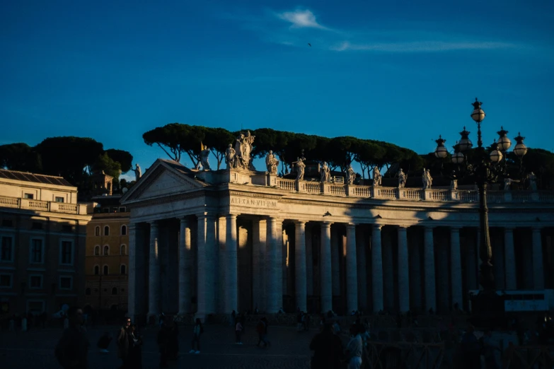 a building with columns, statues and some people standing around it