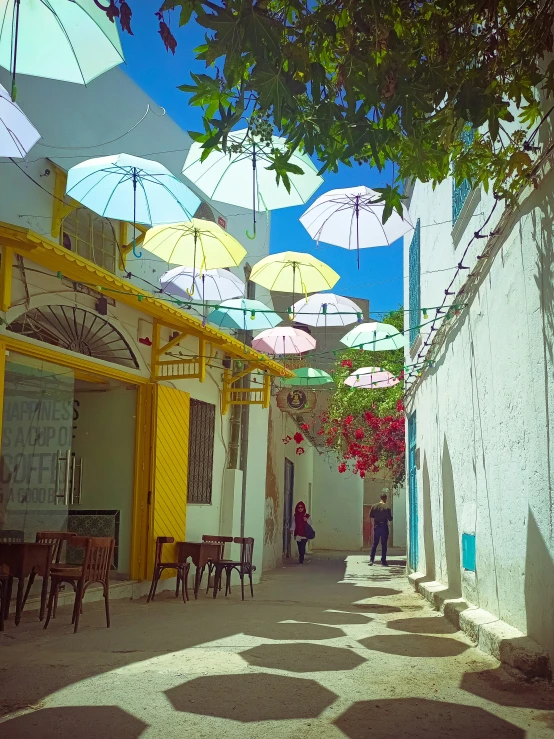 an alley way with white buildings and tables under umbrellas