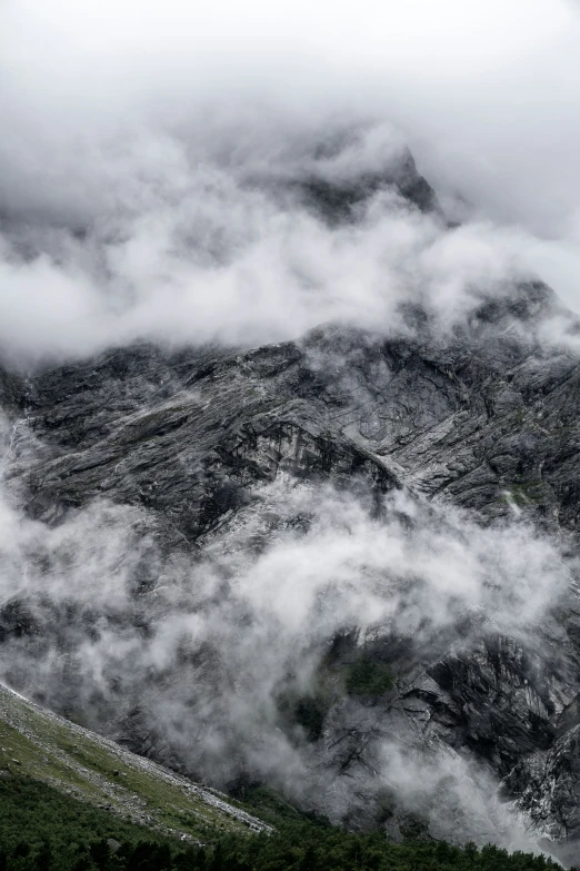 low lying clouds are covering a rocky, green valley