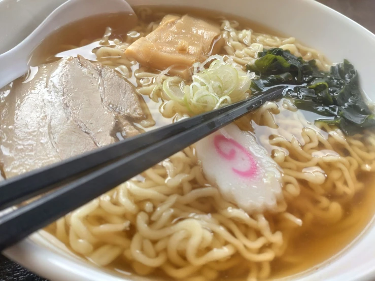 a white bowl of noodles topped with meat and vegetables