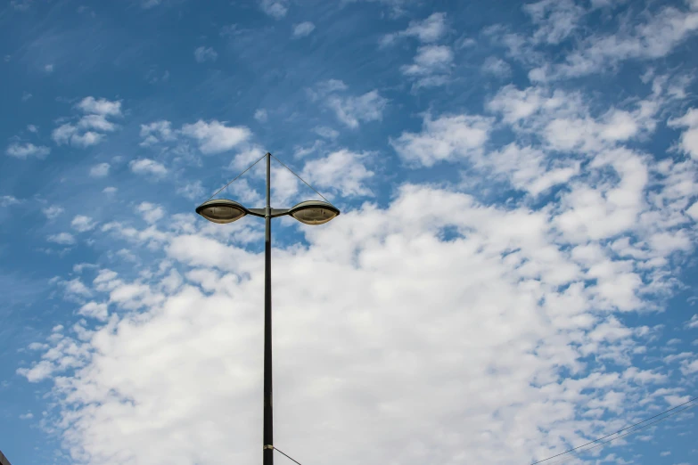 two lamps are next to the pole and are under the cloudy sky