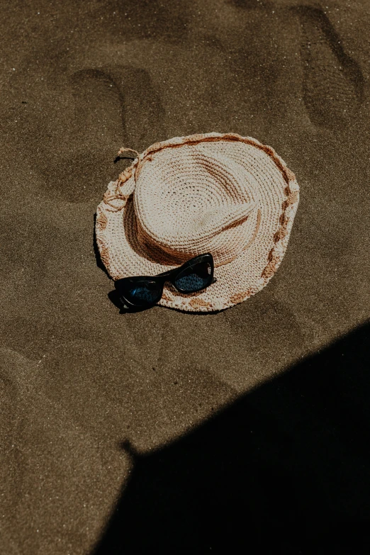 a hat is shown with sunglasses in the sand