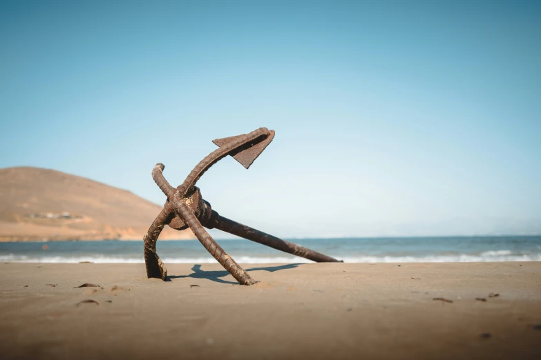 a rusted anchor standing in the sand of a beach