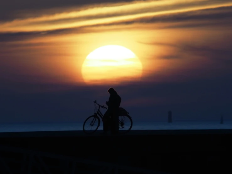 a person walking their bike at sunset by the ocean