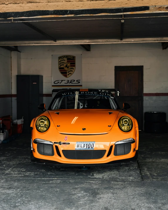 an orange sports car in a garage with a sign saying porsche
