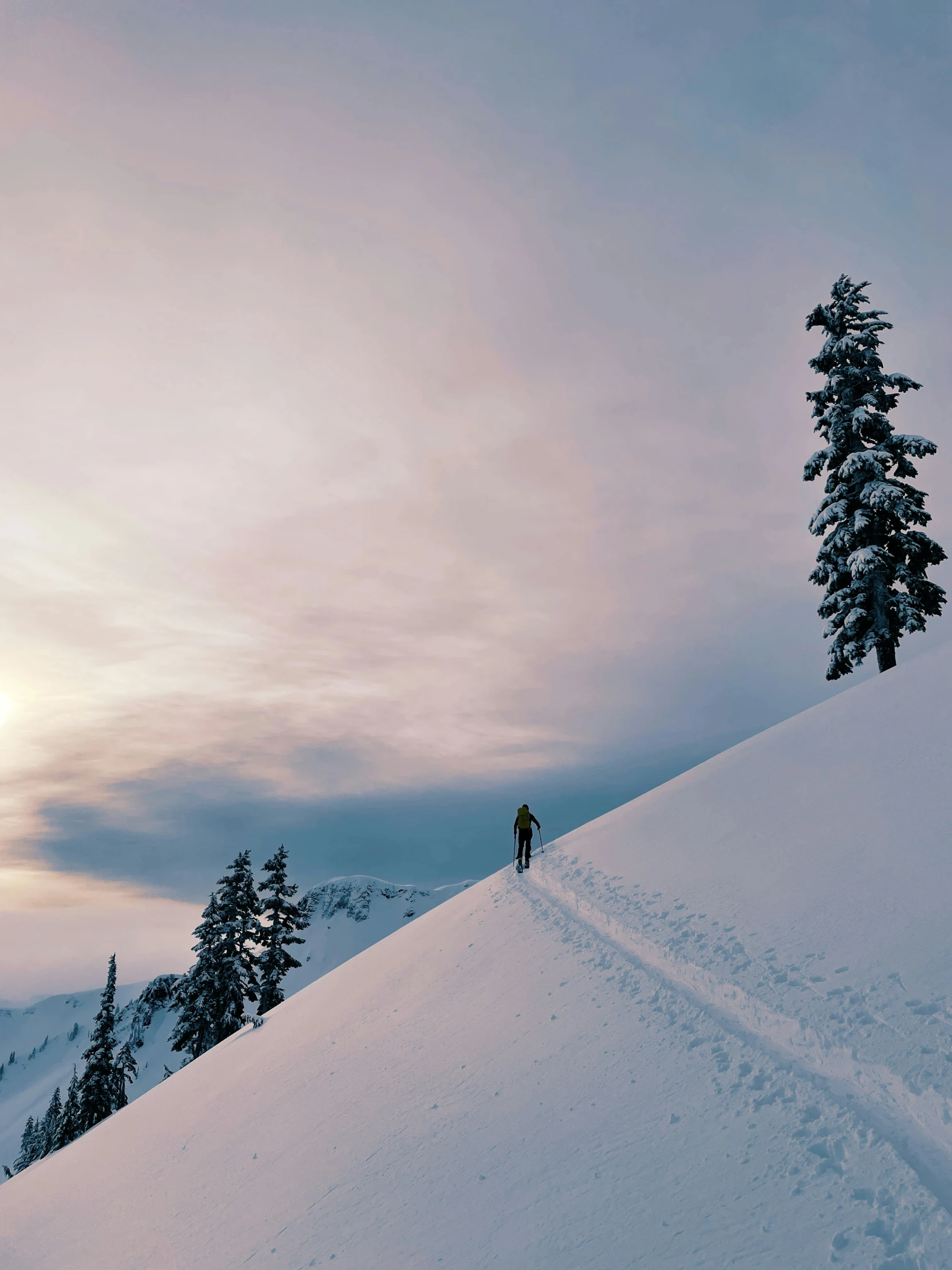 skier walking up a snow covered slope toward the sun