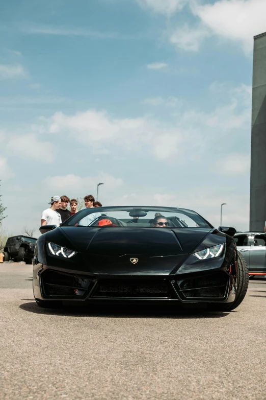 a black sports car sits parked in front of people