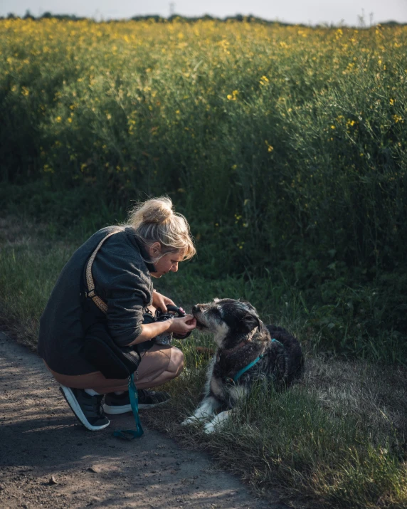 a woman with glasses pets her dog on the side of the road