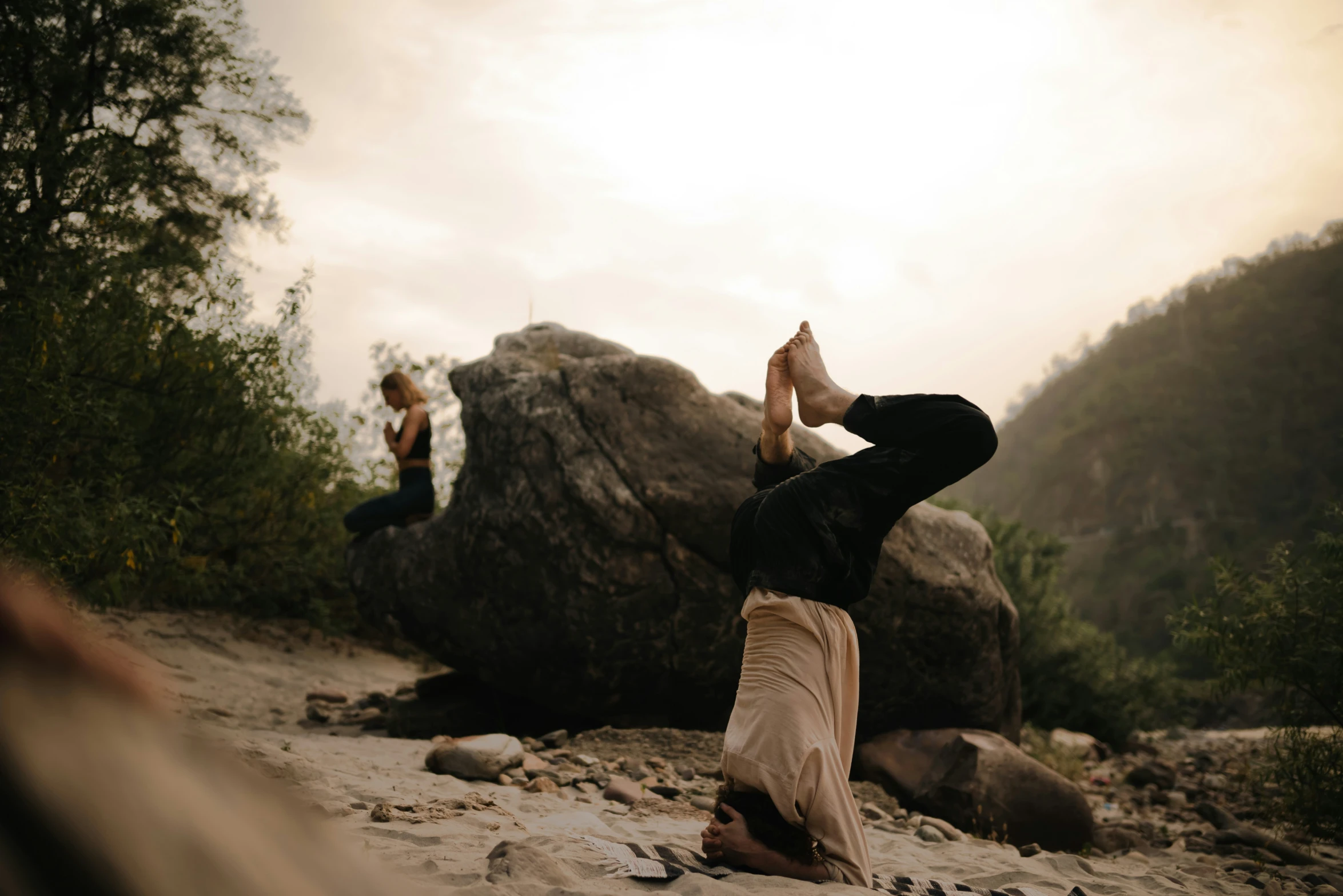 two women are doing yoga on rocks with trees and clouds