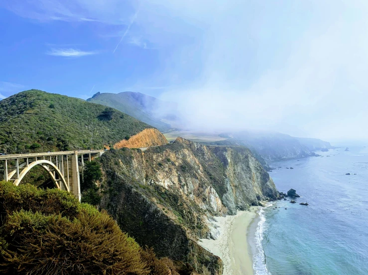 a picture taken from a hillside, a bridge overlooking the ocean