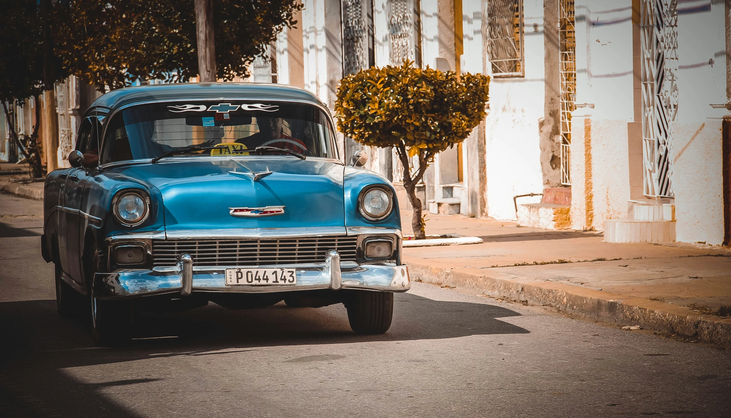 an old blue car driving down the street