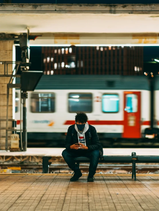 a man with a book sitting on a bench watching a train go by