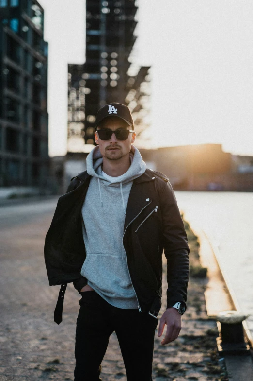 a man wearing sunglasses and a baseball cap walks near water