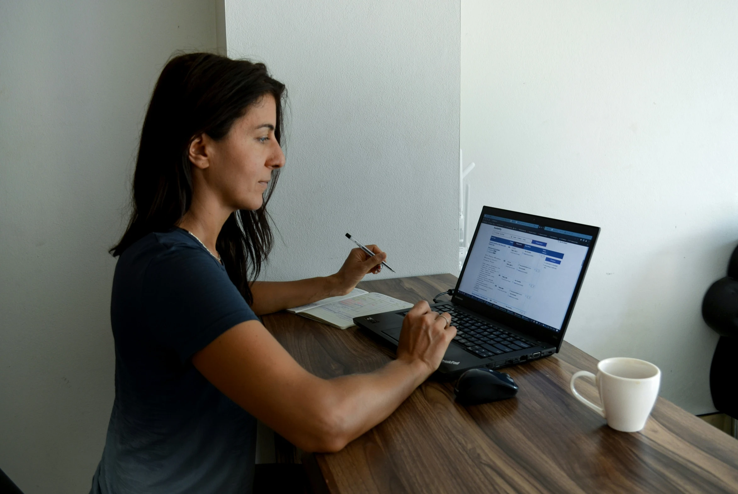 a woman writing on a laptop computer while sitting at a desk