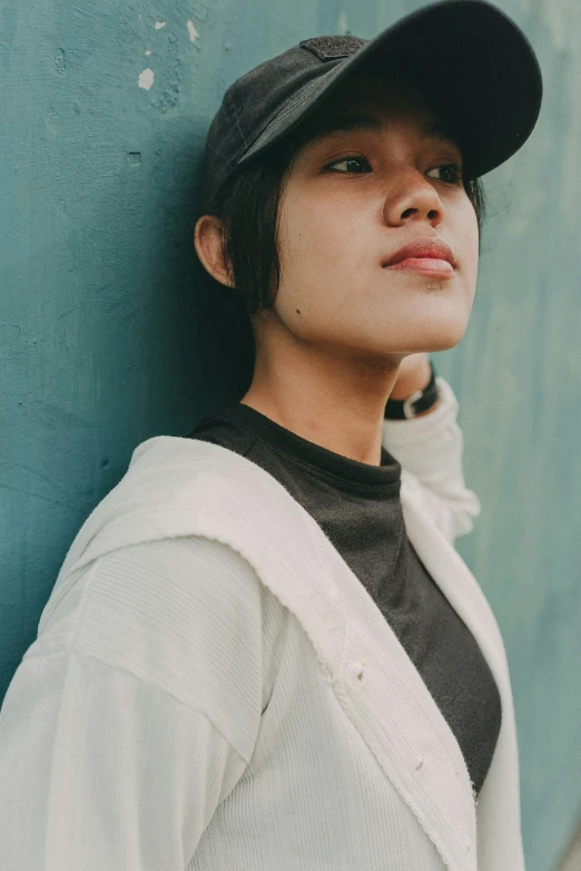 a young man leans against the wall wearing a baseball cap