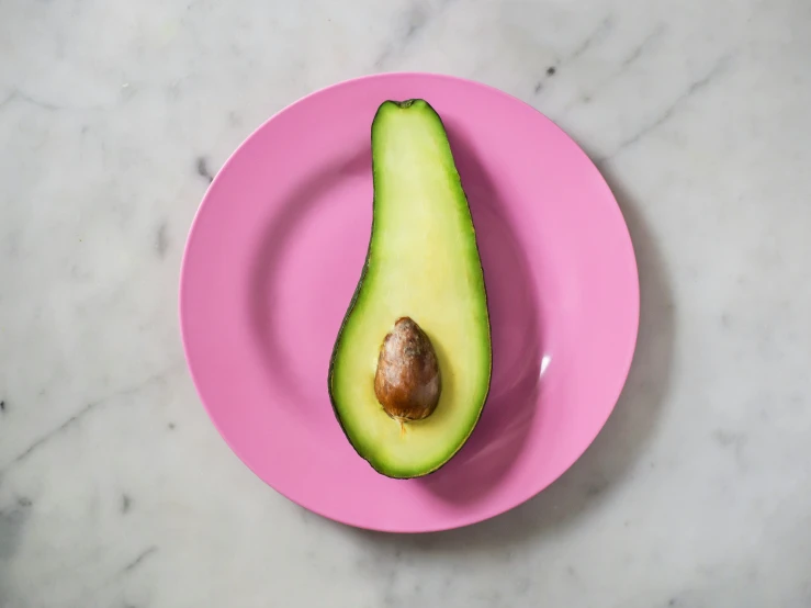 a pink plate topped with an avocado cut in half